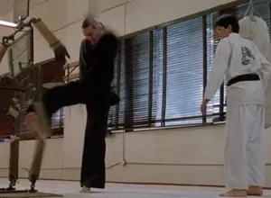 A screenshot of Terry Silver demonstrating rule 1 of the Quicksilver method by kicking the leg of a wooden dummy in the dojo